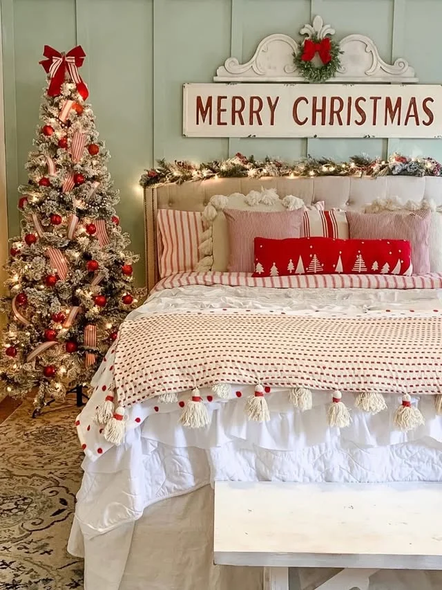 Flocked Christmas tree beside a bed with red tassel bedding and Merry Christmas sign