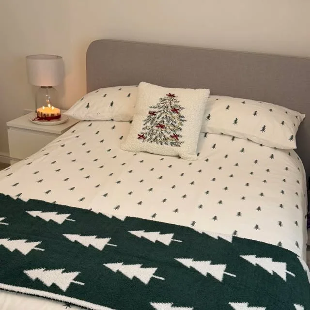 Bed with green Christmas tree print bedding and lit candle on nightstand