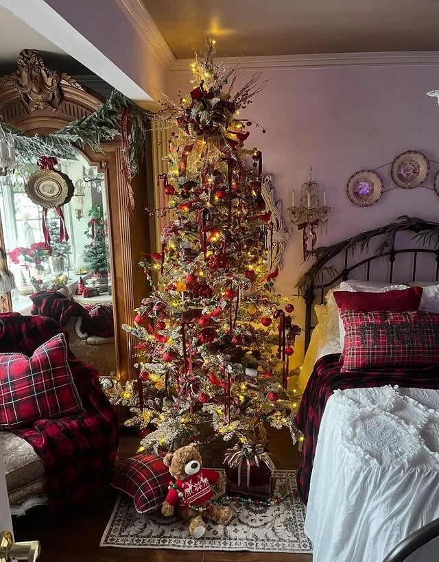 Flocked Christmas tree with plaid ribbons beside a vintage style bed