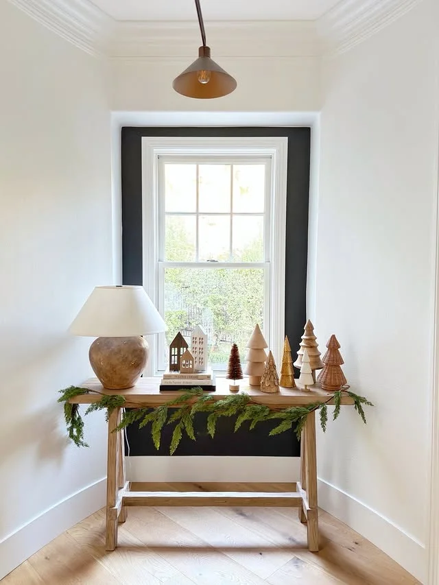 Minimal wood console table with wooden trees and garland under a window