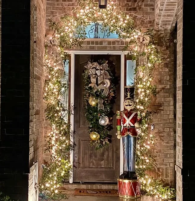 Brick entryway at night with lit garland arch, wreath, and nutcracker figure