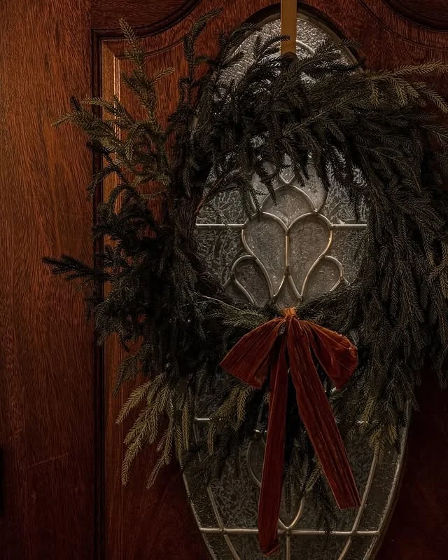 Moody dark cedar wreath with rust velvet bow on a wooden front door