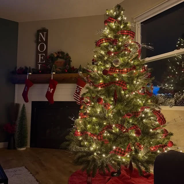 Christmas tree with buffalo plaid ribbon beside a fireplace with stockings