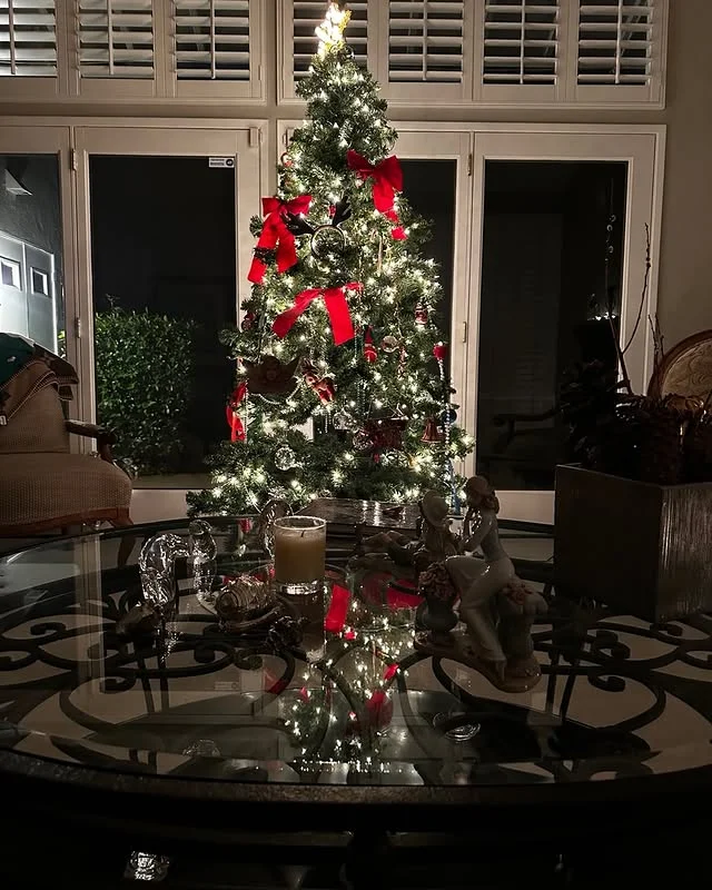 Christmas tree decorated with red bows behind a glass coffee table