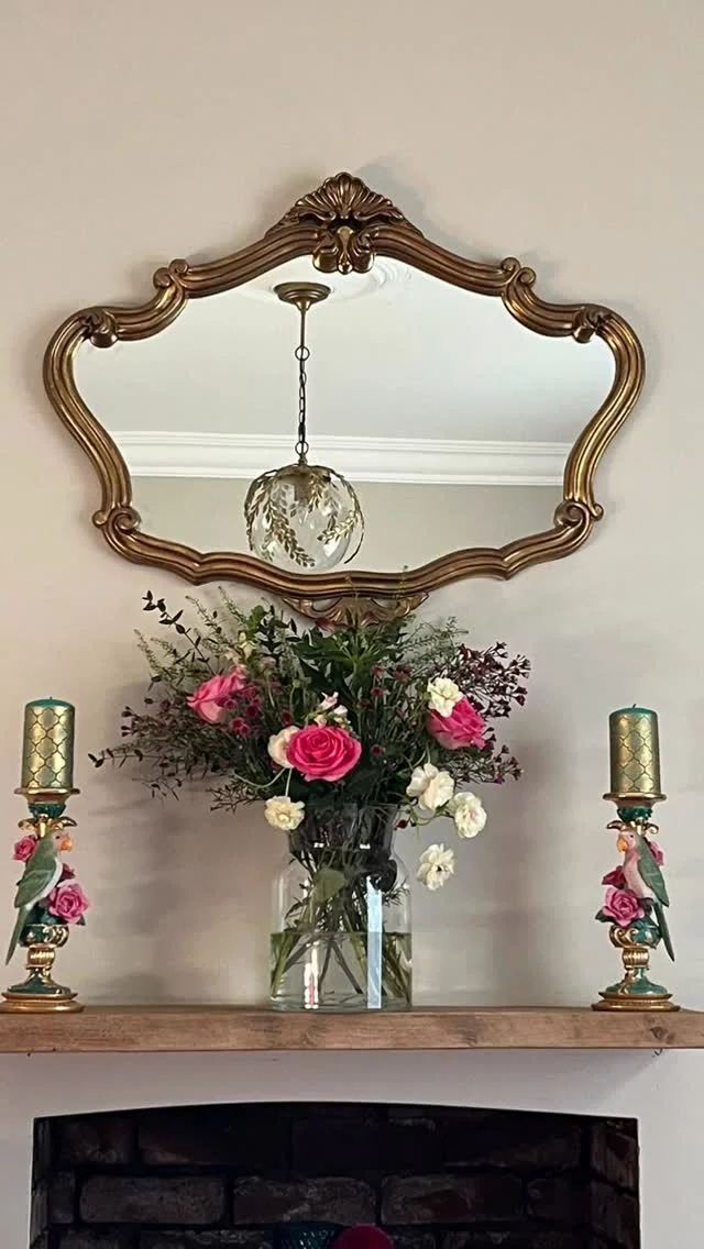 Ornate gold mirror above a mantel with candles and a floral arrangement