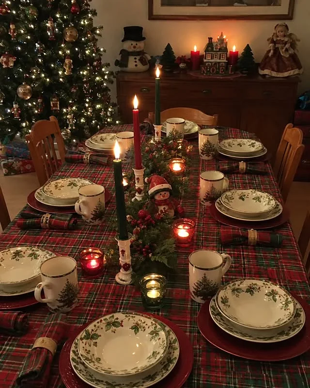 Christmas dining table with red tartan tablecloth, holly patterned plates, and lit candles