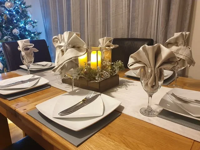 Modern Christmas table with blue tree, folded napkins, and glowing candles