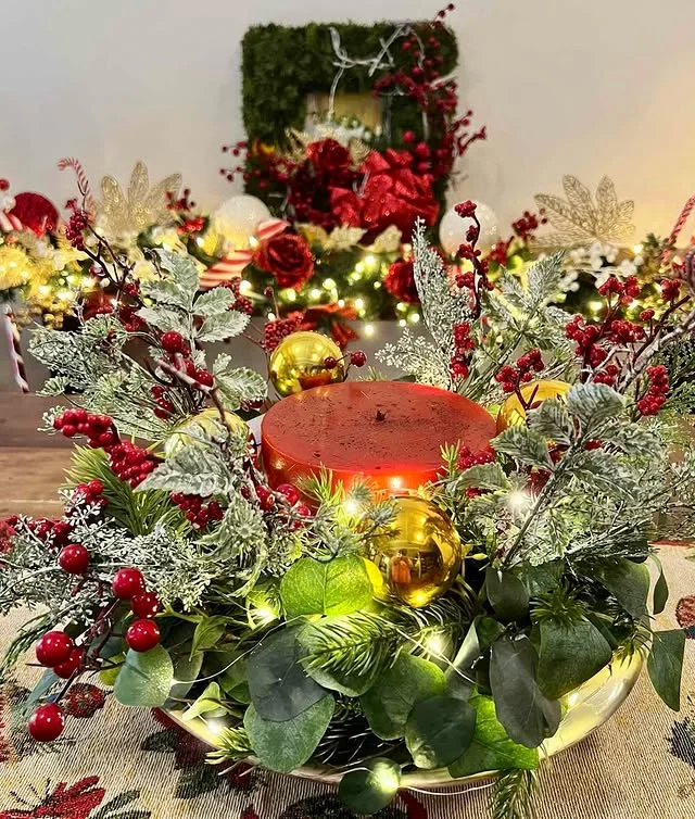 Christmas centerpiece with red berries, gold ornaments, and a lit candle
