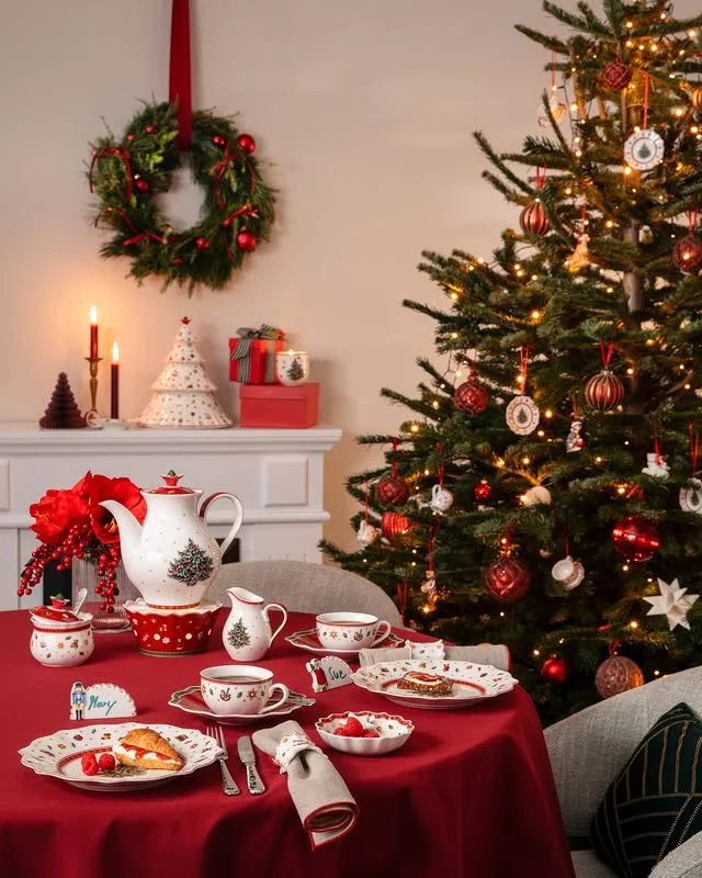 Christmas tea table with red tablecloth, tree-patterned china, and a Christmas tree