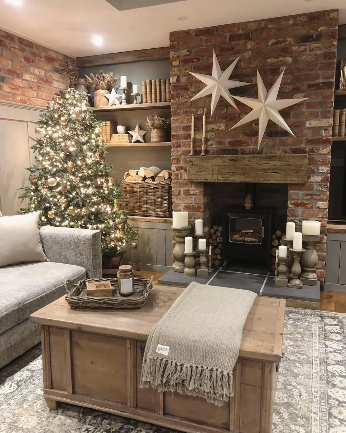 Living room with a lit Christmas tree and exposed brick fireplace with wood mantel