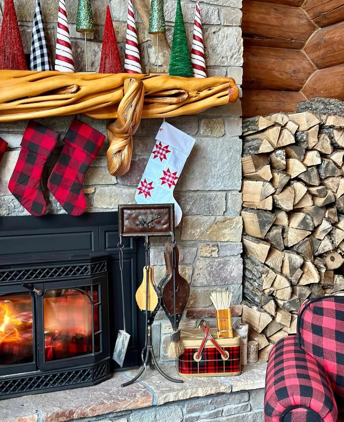Log cabin fireplace with a driftwood mantel, buffalo check stockings and mini trees