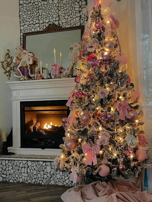 Flocked Christmas tree with pink bows and rose gold ornaments beside a lit fireplace